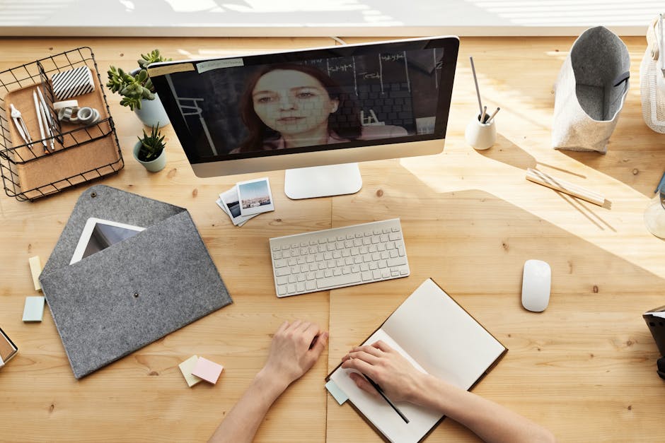A smiling person using a laptop at a bright, sunlit desk.